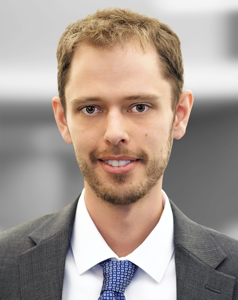 A portrait of Barry Wood, a smiling man with light stubble wearing a suit and tie.