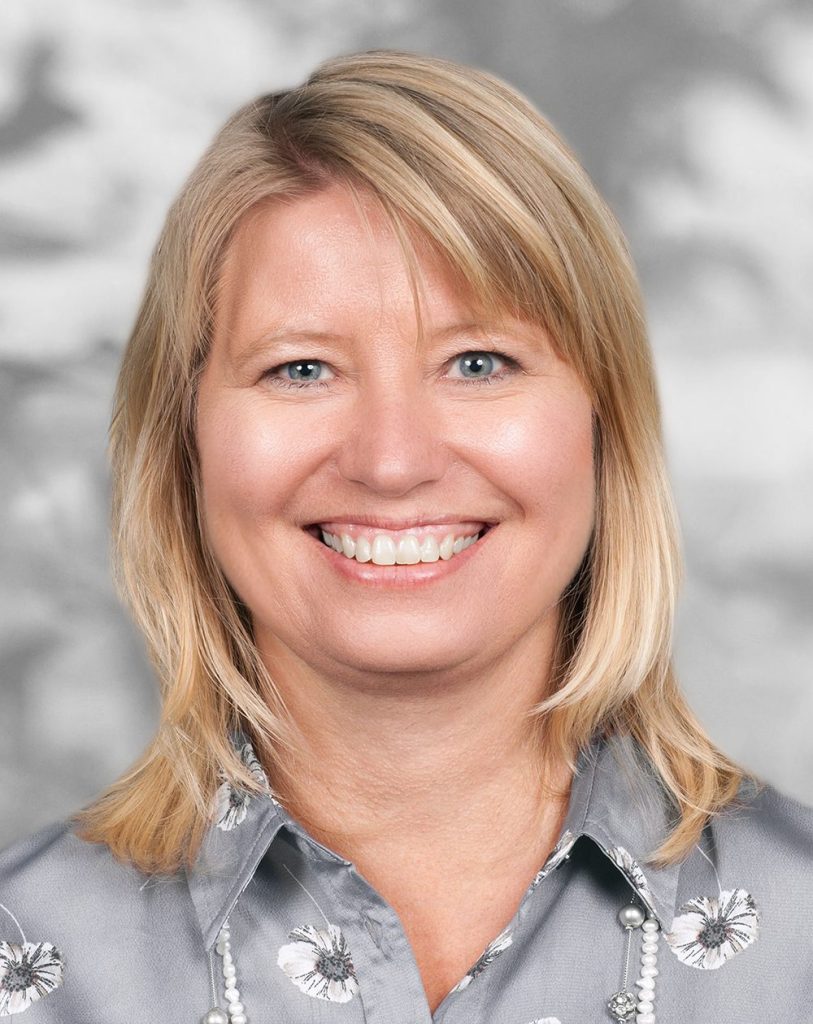 A portrait of Christina Pedersen, a smiling woman with shoulder-length blonde hair against a gray background.