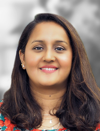 A portrait of Dickshitha Thyagharajon, a smiling woman with shoulder-length hair and a floral top against a blurred background.