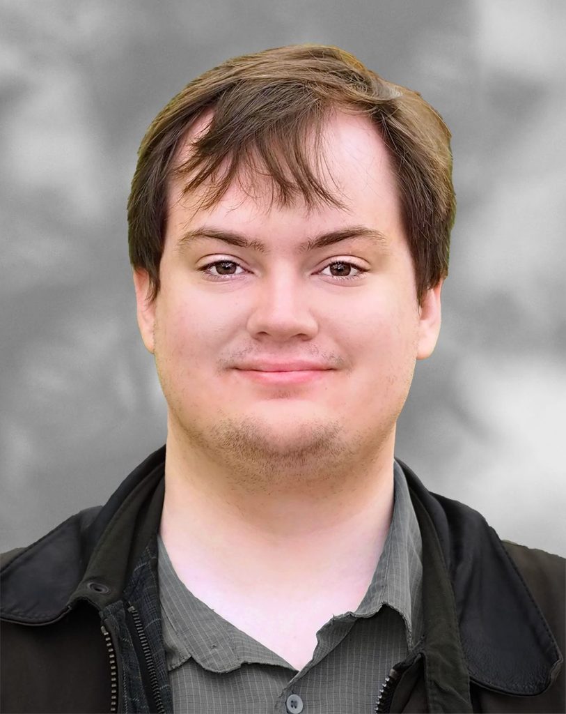 A portrait of Erick Blankenberg, a smiling man with short hair against a blurred gray background.