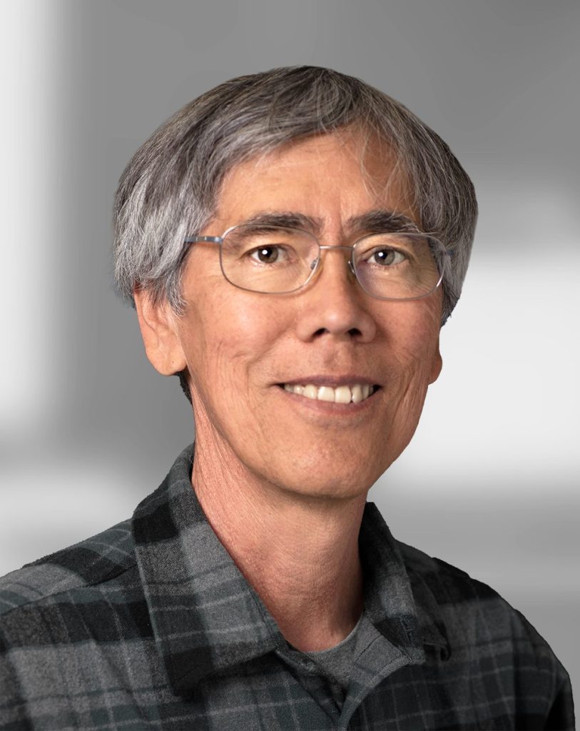 A portrait of Keith Nishihara, a smiling man with gray hair wearing glasses and a plaid shirt.