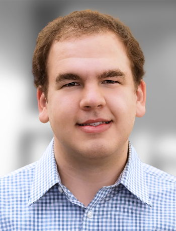 A portrait of Jordan Sweer, a Smiling man with short hair wearing a checkered shirt against a blurred background.