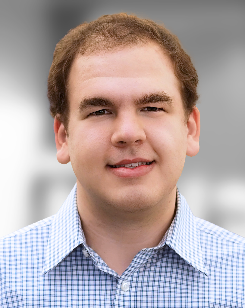 A portrait of Jordan Sweer, a Smiling man with short hair wearing a checkered shirt against a blurred background.