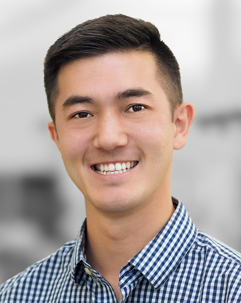 A portrait of Mitchell Parks, a smiling man with short hair wearing a checkered shirt.