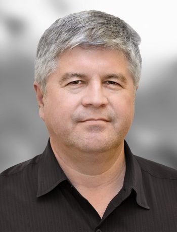 A portrait of Nick Lopez, a man with salt-and-pepper hair and a black shirt.