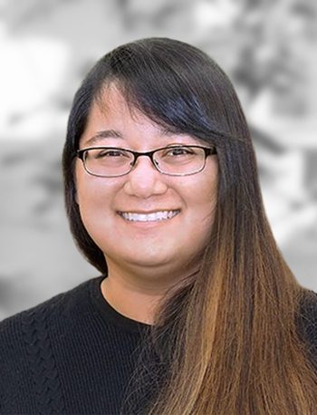 A portrait of Shaheen Jeeawoody, a smiling woman with glasses and long dark hair against a blurred background.