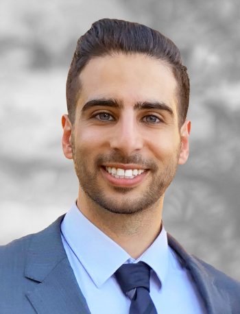 A portrait of Shehadeh Dajani, a smiling man wearing a suit and tie against a blurred background.