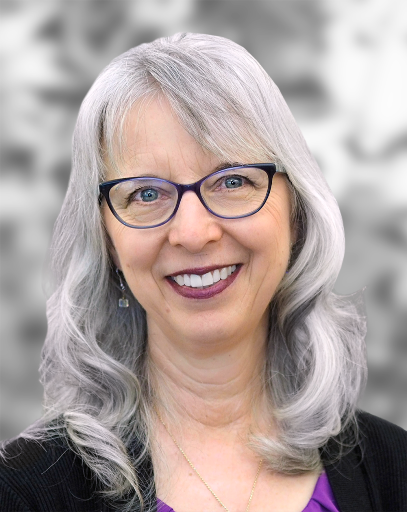 A portrait of Theresa Christian, a smiling woman with gray hair and glasses, wearing a purple top and earrings against a blurred grayscale background.