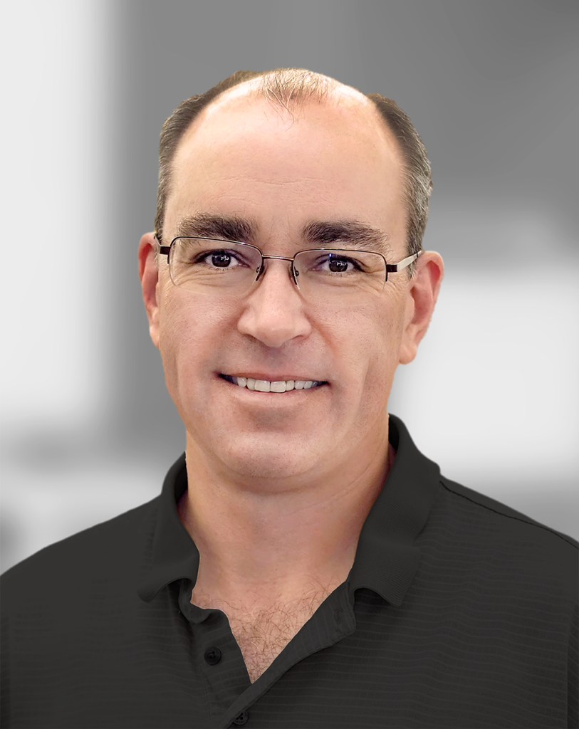 A portrait of Todd Harris, a man with glasses wearing a black shirt against a grey background.