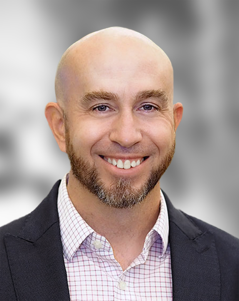 A portrait of Vrad Levering, a smiling man with a beard and plaid shirt smiling against a blurred background.