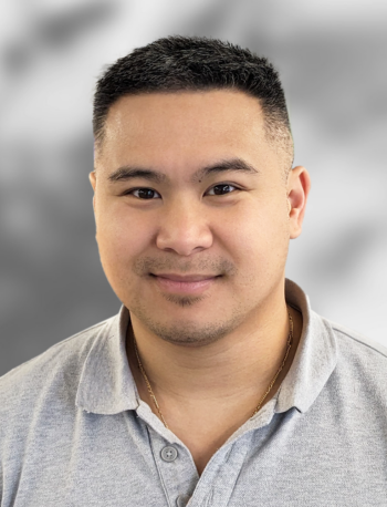 A photo of Son Nguyen wearing a light gray collared shirt, is smiling against a blurred gray background.