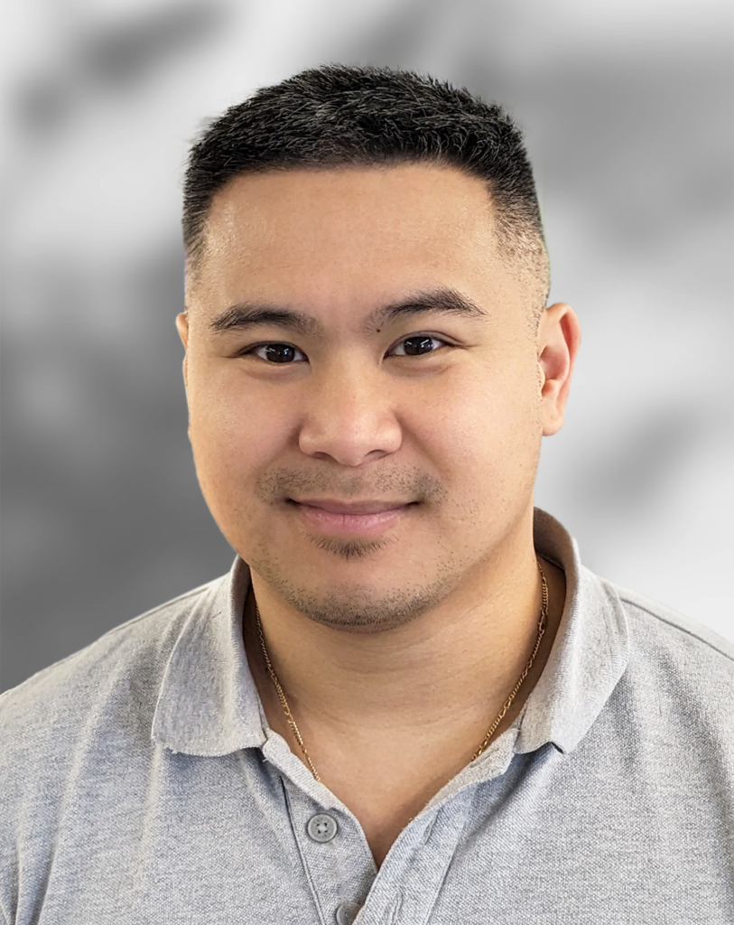 A photo of Son Nguyen wearing a light gray collared shirt, is smiling against a blurred gray background.