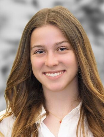 Portrait of Cameran Casale, a person with long, straight brown hair, wearing a white shirt and a necklace, smiling against a blurred background.