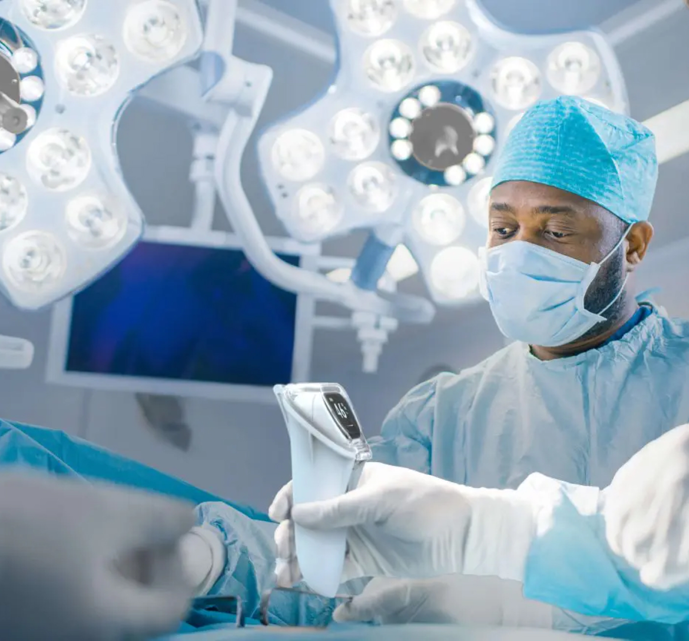 Surgeon in an operating room using a handheld device, surrounded by bright surgical lights.